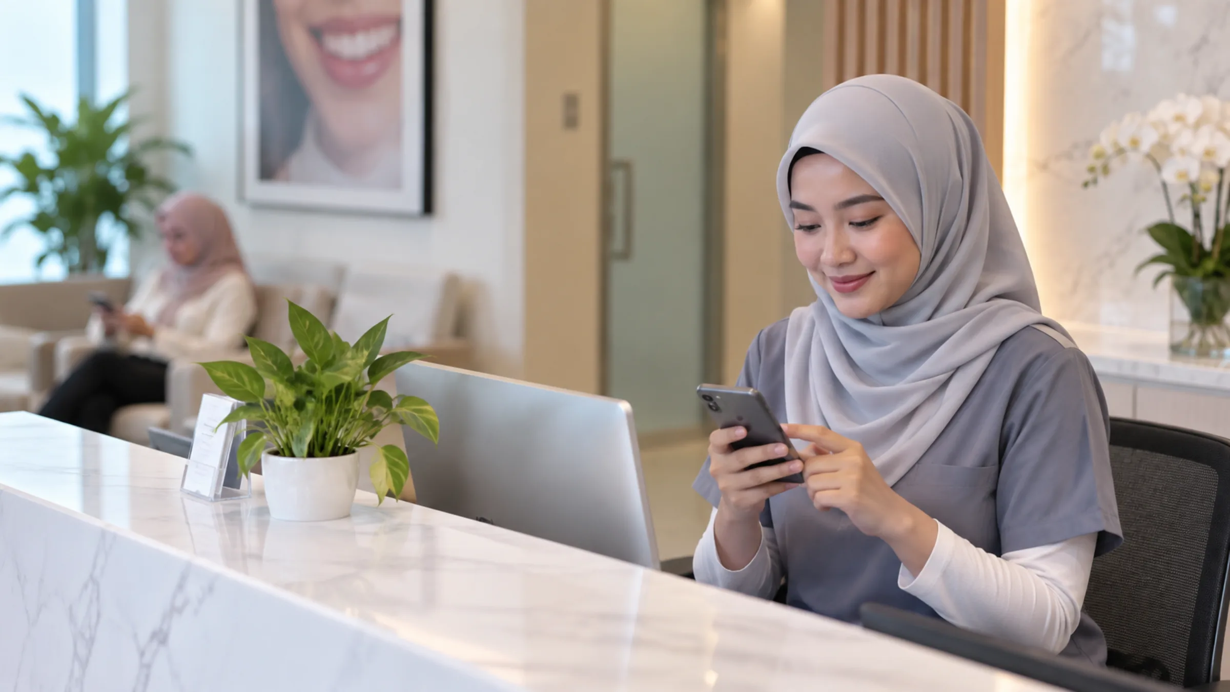 A receptionist in a grey tudung uses her phone behind a bright clinic counter with a plant.